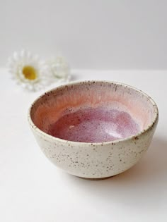 a white and pink bowl sitting on top of a table next to a daisy flower