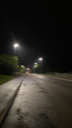 an empty street at night with some lights on the side and trees in the background