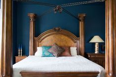 a bedroom with blue walls and white bedding has a wooden canopy over the bed