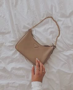 a woman's hand holding onto a beige purse on top of a white sheet