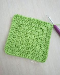 a crocheted square with a purple knitting needle next to it