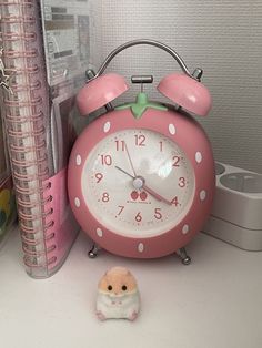 a pink alarm clock sitting on top of a desk next to a small toy hamster