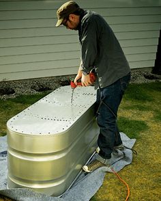 a man working on an outdoor hot tub in the grass with a hose attached to it