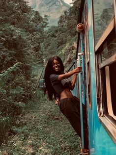 a woman leaning out the side of a train window while standing next to a lush green forest