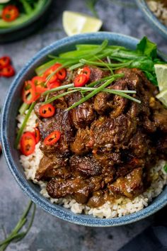 a blue bowl filled with rice, meat and veggies next to lime wedges