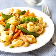 a white plate topped with pasta and veggies on top of a blue table cloth