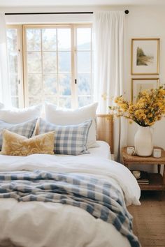 a bed with blue and white plaid pillows in front of a large window filled with yellow flowers