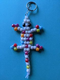 a cross made out of candy beads on a blue surface with a keychain