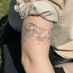 a woman with a tattoo on her arm is sitting in the grass and looking down