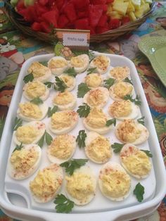 an assortment of deviled eggs on a platter with parsley and tomatoes in the background