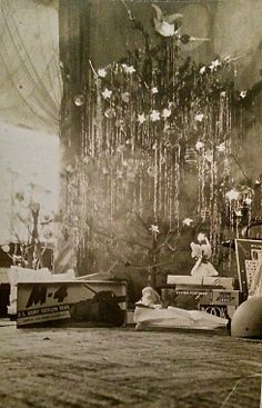 an old black and white photo with many items on the floor in front of a christmas tree