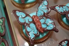 cupcakes decorated with blue and brown icing are in a muffin tin