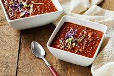 two white bowls filled with chili and garnish on top of a wooden table