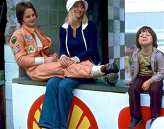 two women and a child sitting on top of a carnival ride bench with their feet in the air