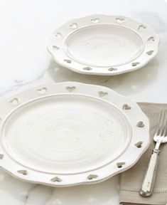 two white plates with hearts on them next to a silver fork and knife, sitting on a marble table