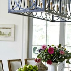 a dining room table with flowers and fruit on it in front of a chandelier