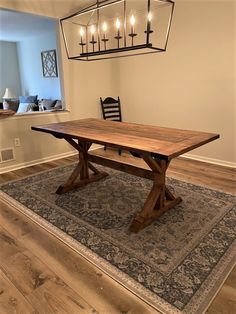 a wooden table sitting on top of a rug under a chandelier above a light fixture