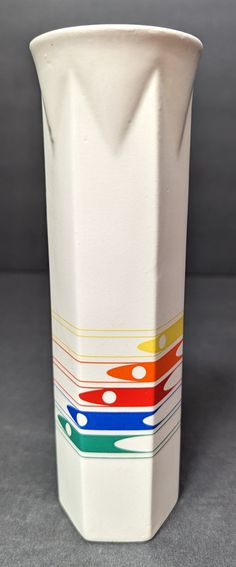 a white vase with multicolored lines on the bottom and sides, sitting on a gray surface