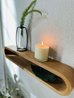 a candle is sitting on a shelf next to a vase with a plant in it