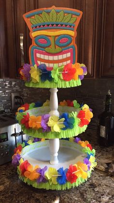 three tiered cake stand decorated with paper flowers and a tiki mask on top