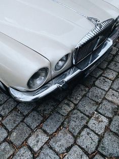 an old white car is parked on the cobblestone street in front of a building