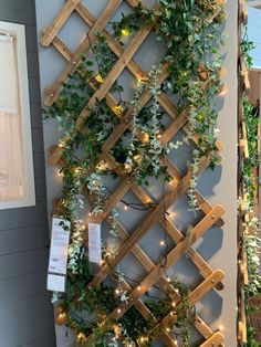 a wooden trellis with lights and greenery hanging on it's side wall