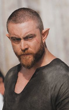 a close up of a person with a beard and wearing a black t - shirt