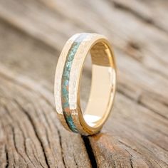 a gold ring with blue and green wood inlays on it sitting on a piece of wood