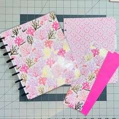 three notebooks with pink and yellow flowers on them next to a cutting board, scissors and ruler