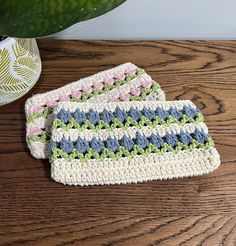 two crocheted dishcloths sitting on top of a wooden table next to a potted plant