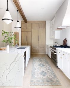 a kitchen with white cabinets and marble counter tops, along with an area rug in the middle