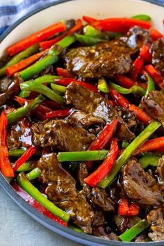 beef and peppers stir fry in a white bowl on a blue tablecloth with a fork