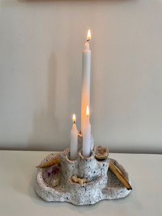 two white candles sitting on top of a rock with seashells and shells around it