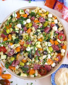 a bowl filled with pasta salad next to some crackers and vegetables on a table