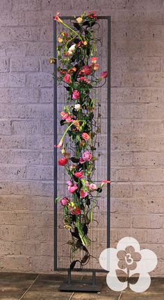 a tall metal planter filled with flowers on top of a wooden floor next to a brick wall