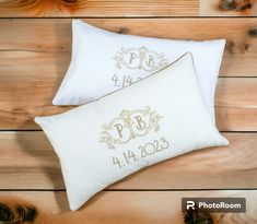 two white pillows with gold monogrammings on them sitting on a wooden floor