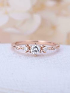 the three stone engagement ring is set on top of a white cloth with flowers in the background