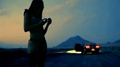 the silhouette of a woman standing next to a car at night with mountains in the background