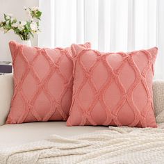 two pink pillows sitting on top of a white couch next to a vase with flowers