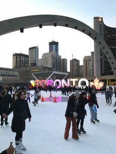 several people skating on an ice rink in front of the toronto sign at dusk with buildings in the background