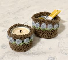 two crocheted baskets sitting on top of a bed with a candle in it