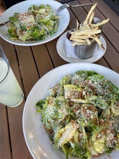 two white plates filled with salad and french fries on a table next to a glass of milk