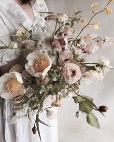 a woman holding a large bouquet of flowers in her hands and wearing a white dress