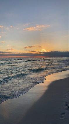 the sun is setting over the ocean with footprints in the sand and waves coming ashore