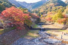 some people are walking around in the mountains near a river and trees with red leaves