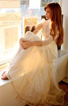 a woman in a white dress sitting on a window sill