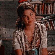 a woman sitting in front of a bookshelf holding a blue bottle and looking at the camera