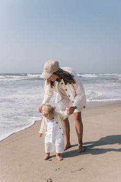 a woman and child on the beach with waves in the background, holding their hands