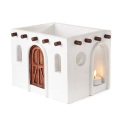 a small white candle holder with a door and window on the front, holding a lit candle