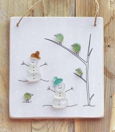 two snowmen are hanging from a string on a white plaque with birds perched on it